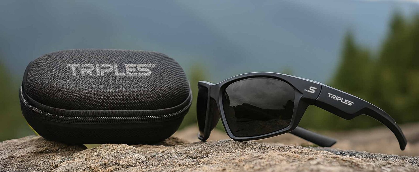 Gafas de sol TRIPLES con estuche sobre superficie natural en contexto outdoor